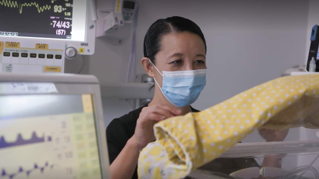 A female doctor stares into an incubator in a hospital.
