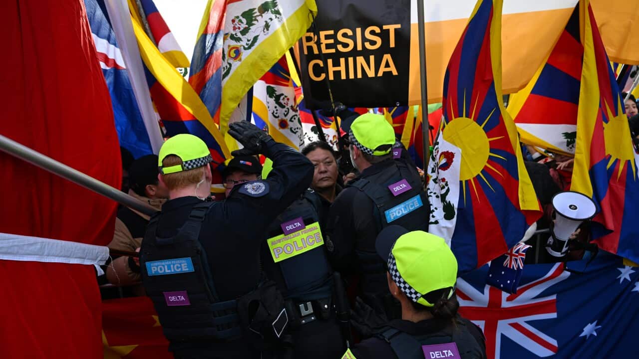The back of police officers dealing with protestors holding up "resist china" banners and Australian as well as Chinese flags.
