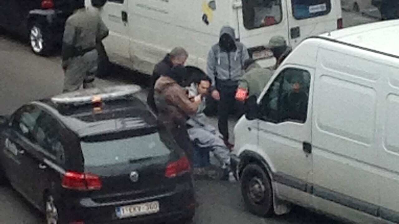 An unidentified man believed to be connected to Salah Abdeslam, is detained by police during a raid in the Molenbeek neighbourhood of Brussels.