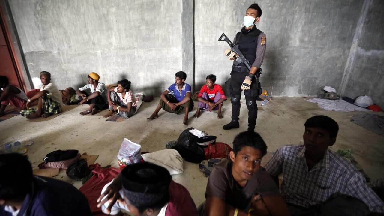 Police officer stands guard in front of migrants at a temporary shelter in Kuala Langsa, Aceh, Indonesia, 17 May 2015. (EPA/HOTLI SIMANJUNTAK)