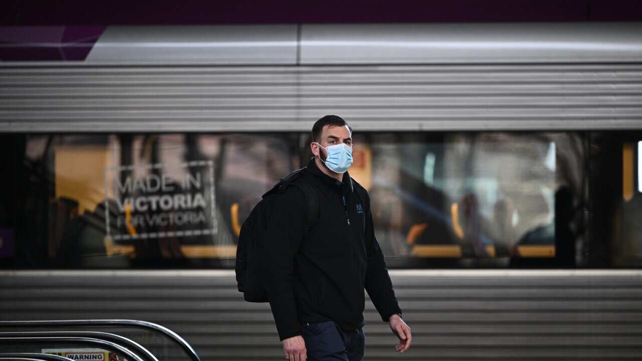 A man with a facemask walks by a train.