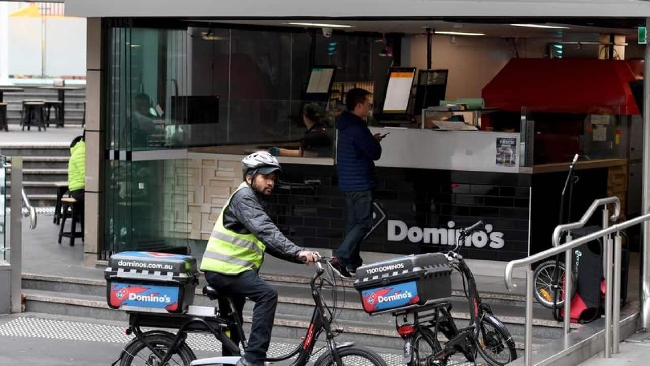A delivery person on bicycle departs a Domino's Pizza store