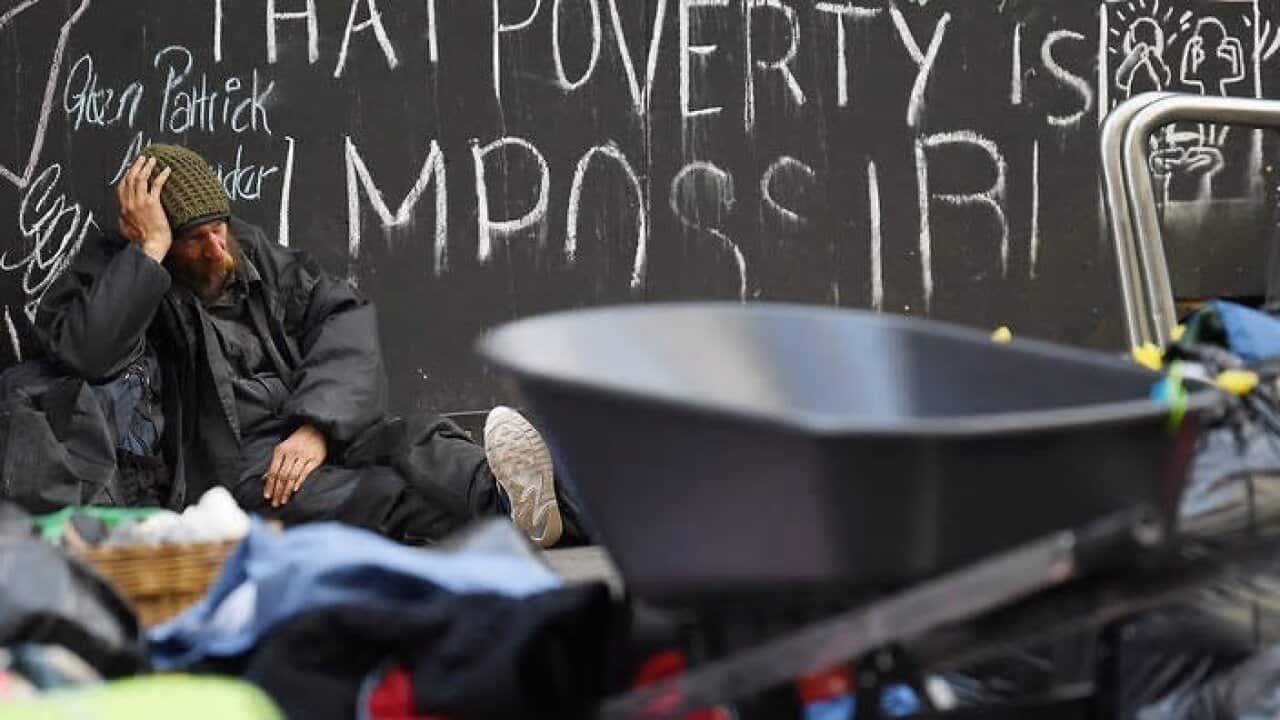 A homeless man sits on the ground as others pack away their belongings and prepare to leave Tent City in Martin Place in Sydney (AAP)