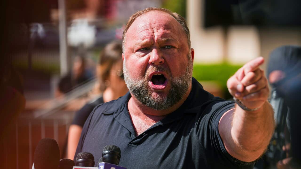 Alex Jones pointing finger and speaking into microphones in front of media