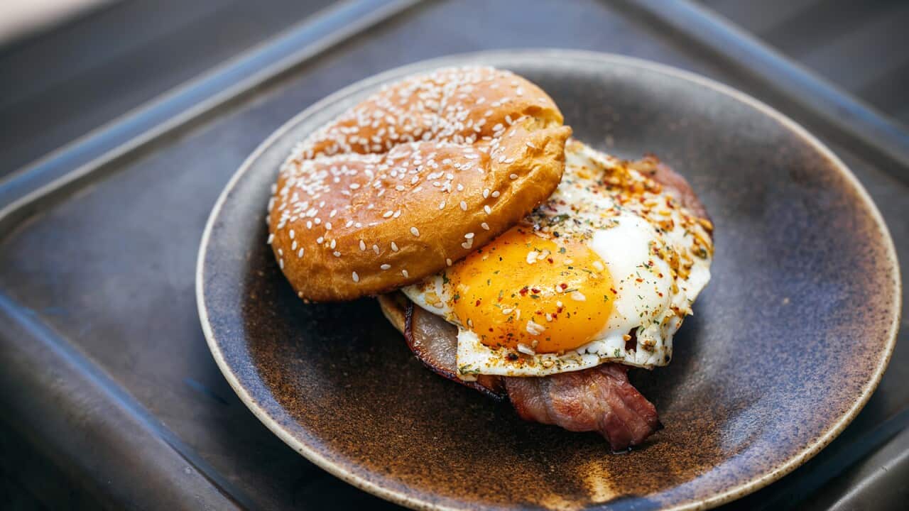 A bacon and egg roll sits on a brown plate. A prinking of seasoning can be seeon on the egg.