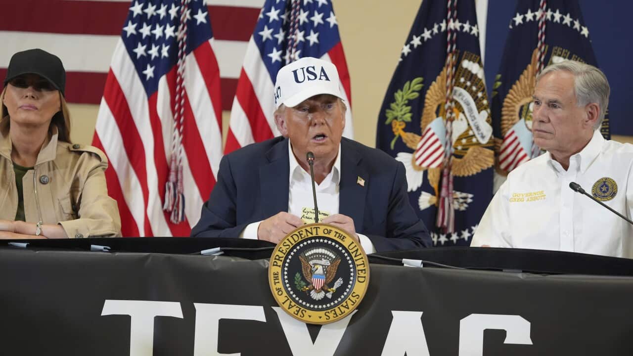 President Donald Trump speaks into a microphone in front of a table with the US presidential seal and the word "Texas" on a large banner. He is flanked by Melania Trump and Texas Governor Greg Abbott.