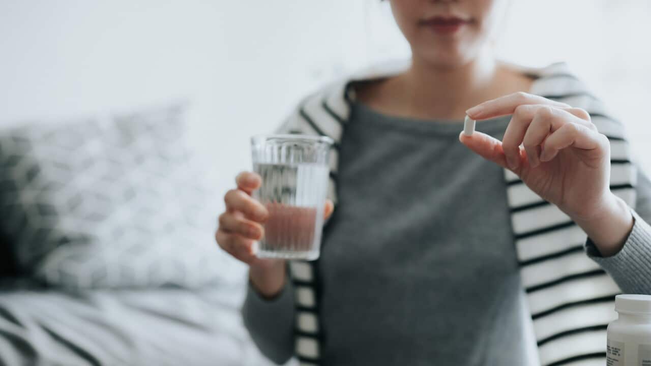 Young Asian woman taking medicines with a glass of water at home, with a pill bottle by the side. Medicine, healthcare and people concept