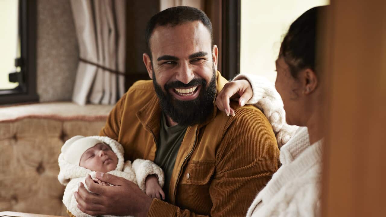Father laughing while carrying daughter and looking at mother in camper van