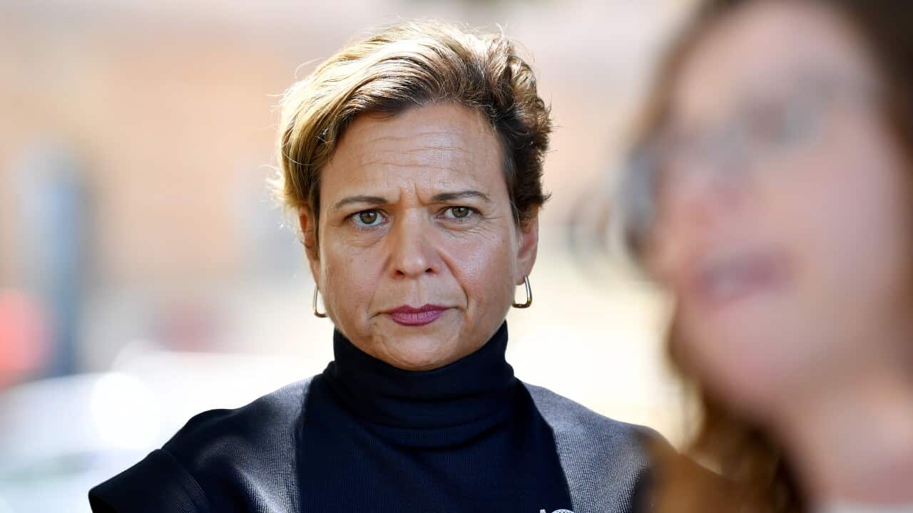 A woman with short hair and wearing a black top, looking serious.