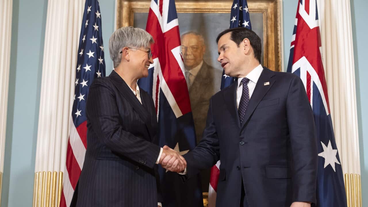 A woman in a suit shakes hands with a man in a suit with Australian and US flags behind them.