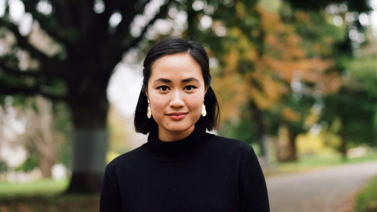 Young Asian woman in park looking at camera and smiling slightly.