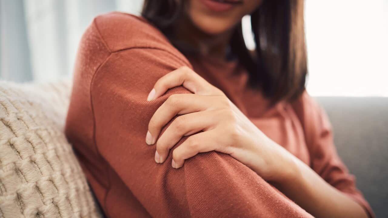 Close up of a young woman holding her arm and suffering with pain while sitting in the living room at home. Mixed race woman holding her arm in pain due to injury or arthritis