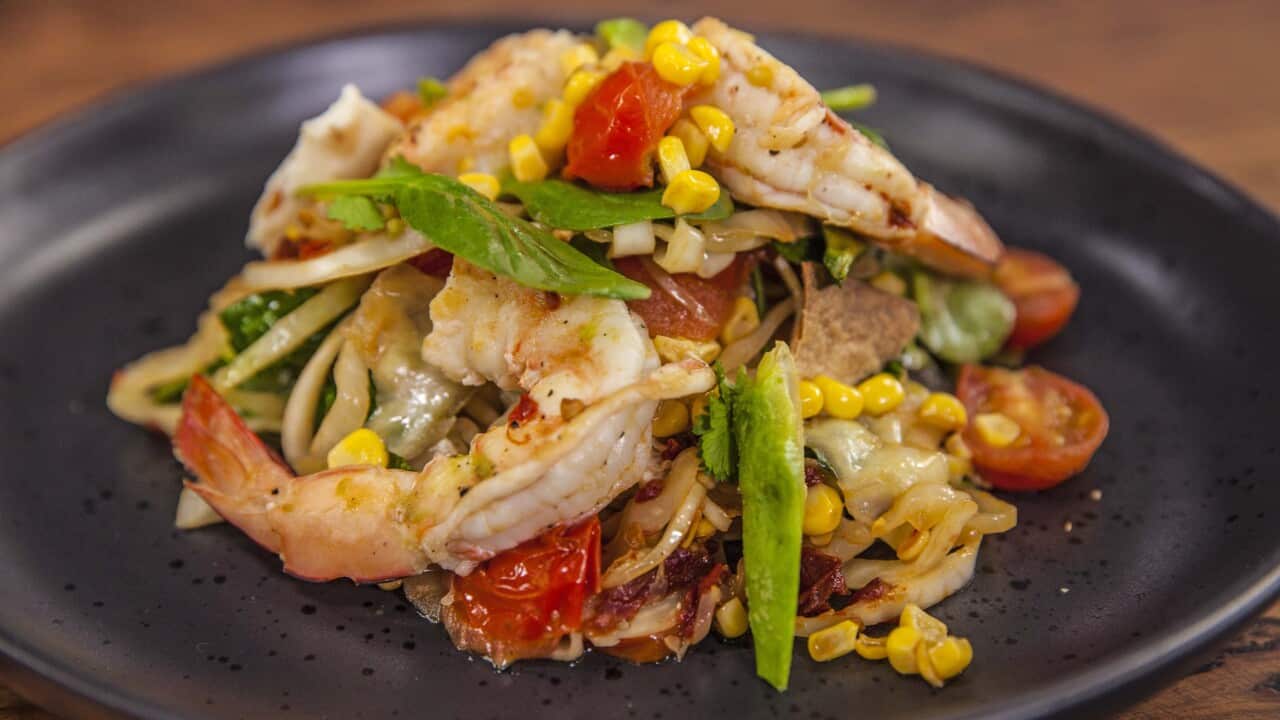 A colouful prawn, cabbage, avocado and tomato salad sits piled on a dark plate.