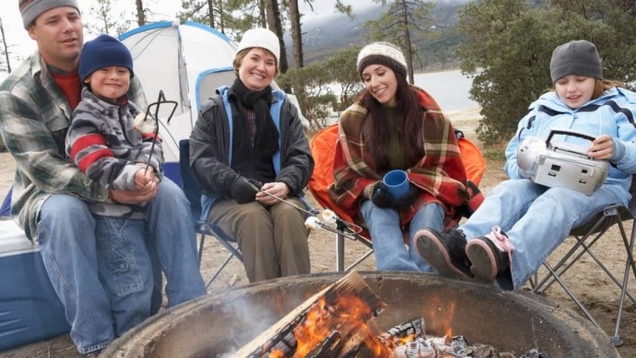 Family with two children (7-12) sitting around campfire (portrait)