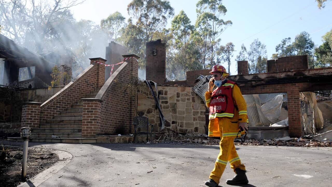 A member of the CFA walks past a destroyed house after a fast moving bushfire took out at least 3 homes in the Melbourne north east suburb of Warrandyte, Monday Feb. 10, 2014. A total fire ban is in place across Victoria during the heat wave temperatures