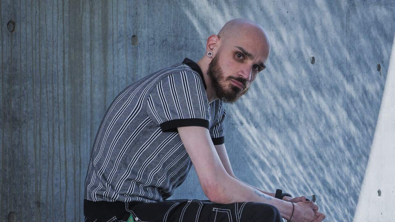 A man sits on a wooden bench outdoors. 