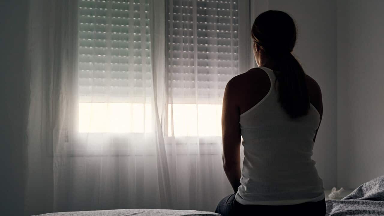 Rear view of an unrecognizable abused woman sitting on her bed looking out the window.
