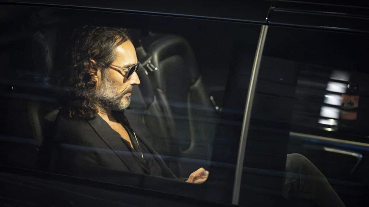 Hollywood actor Russell Brand sitting inside a car, dressed in black and wearing sunglasses.