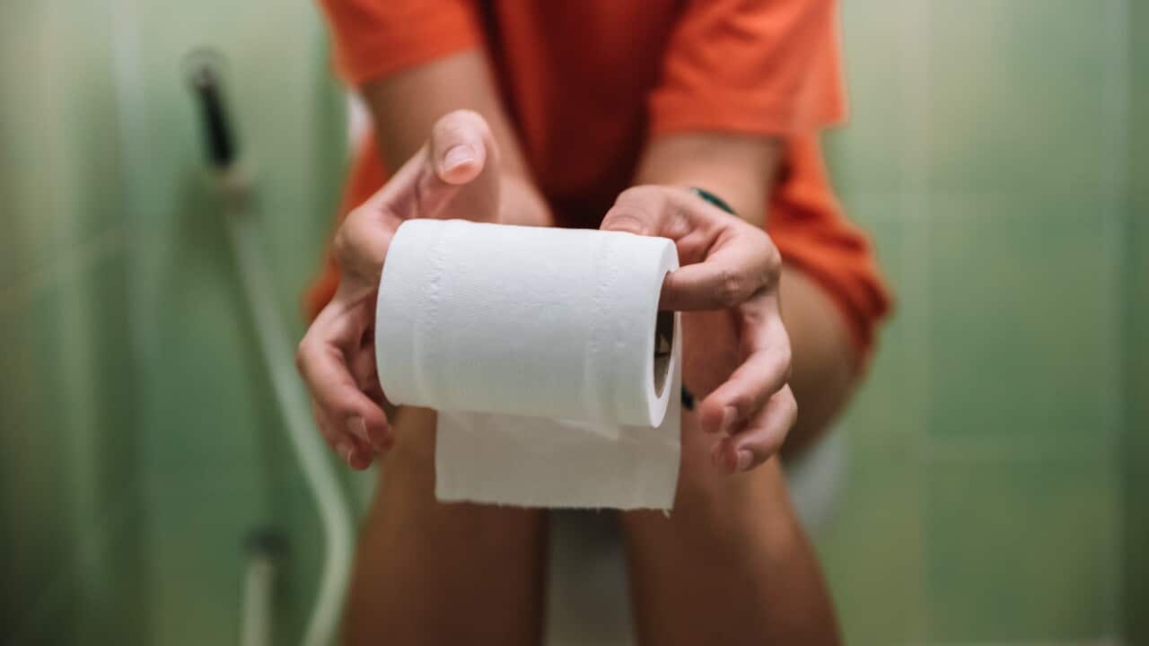 Woman sitting on toilet holding toilet paper roll