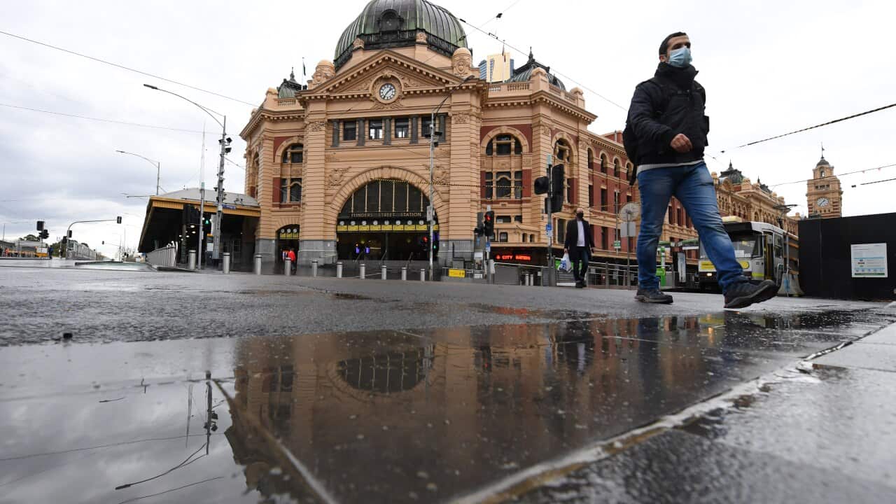People wearing face masks walk across the road at Flinders Street Station in Melbourne.