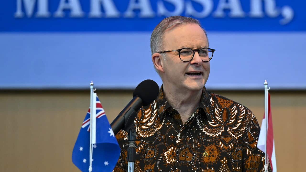 Anthony Albanese wears a brown batik shirt, standing on a podium. In front of him is a mini Australian and Indonesian flag.
