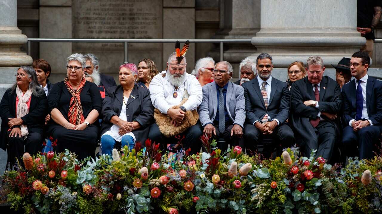 A large group of people sitting on chairs in front of a row of flowers.