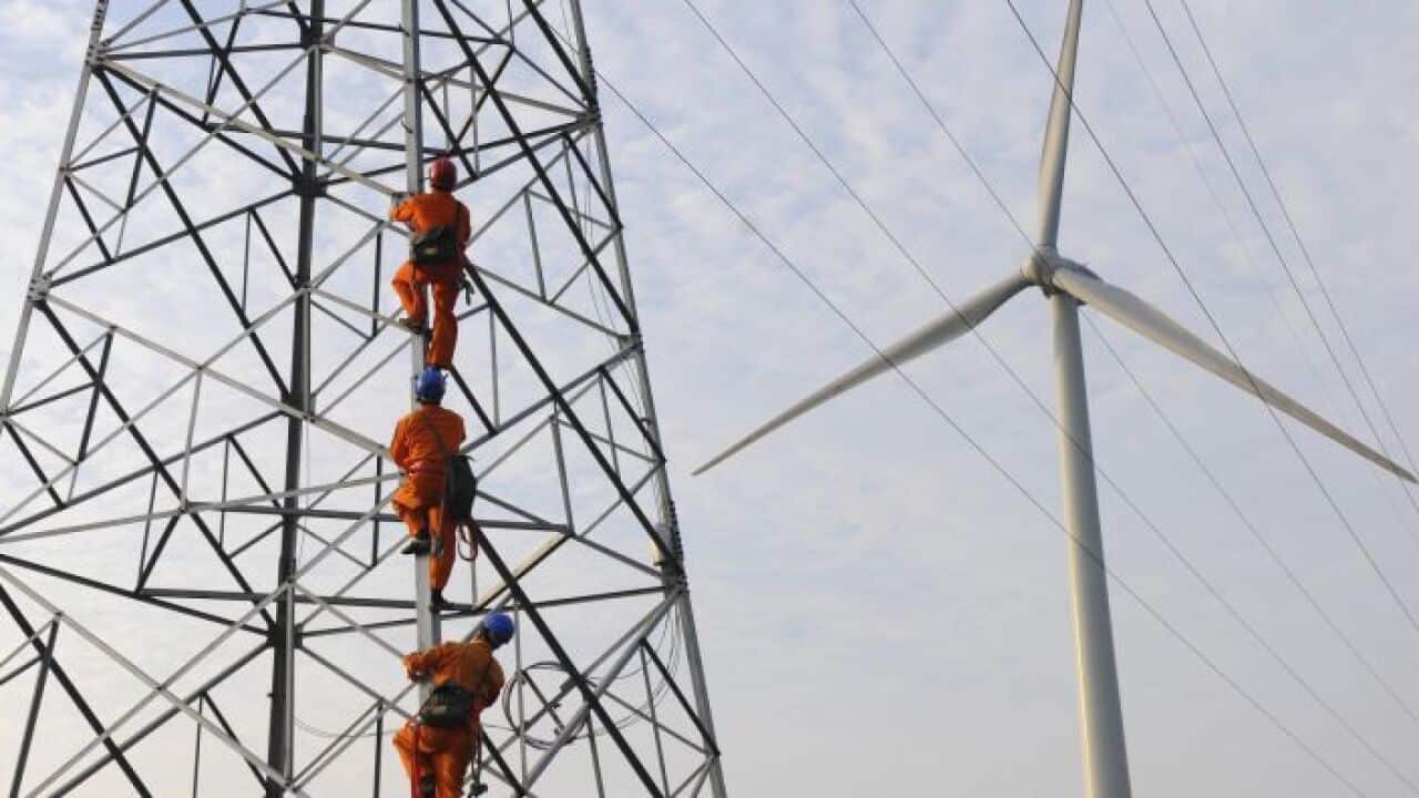 Employees climb up an electricity pylon next to a windmill.