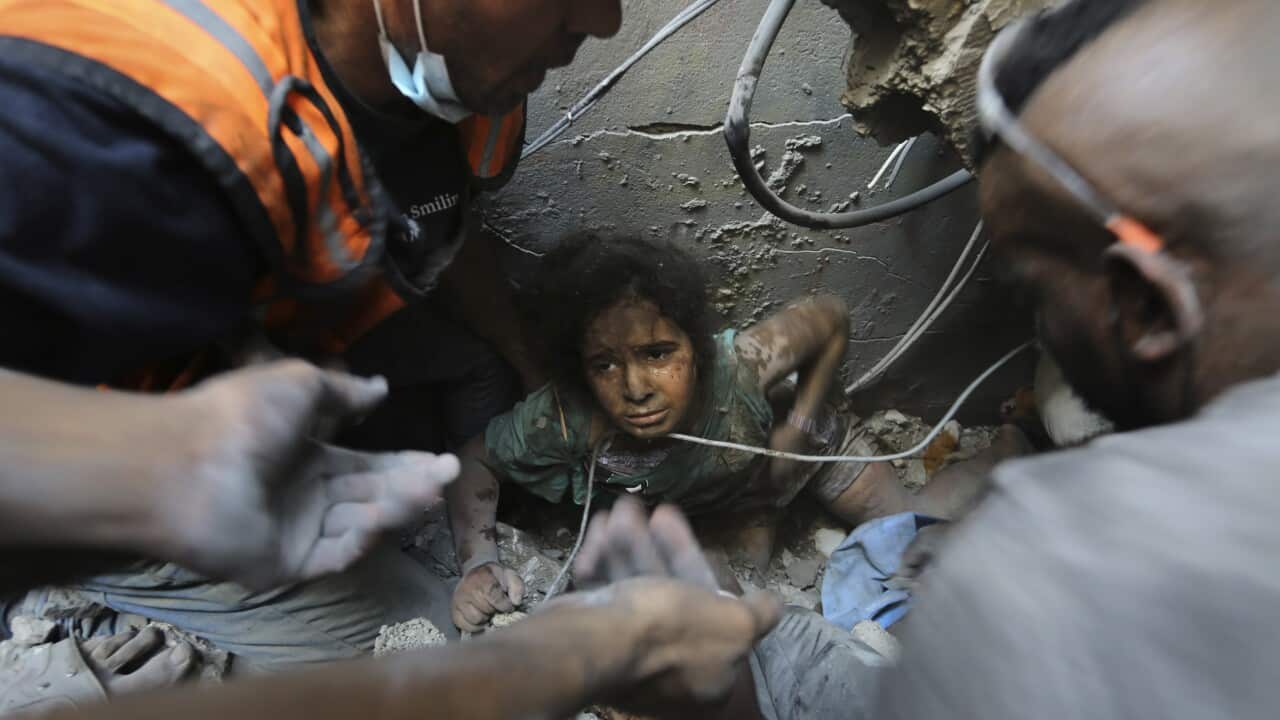 A close up of a girl, covered in soot, being lifted from rubble.