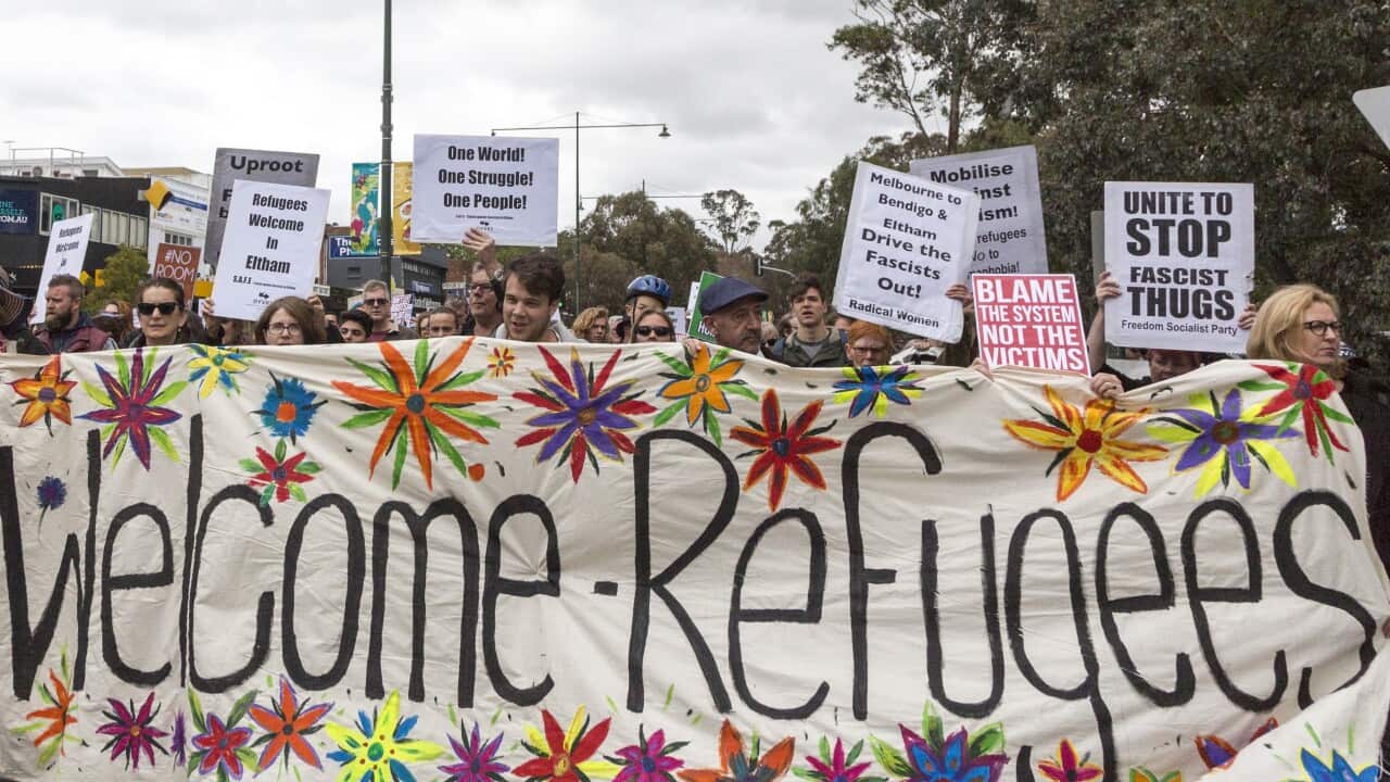 Refugee advocates carry a banner calling for refugees to be welcomed, with some also holding posters.