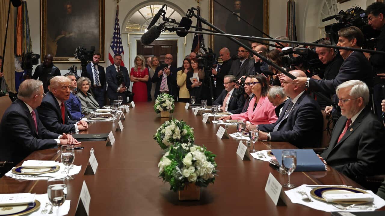 Former prime minister Kevin Rudd sits at a table across US President Donald Trump and Prime Minister Anthony Albanese, with a delegation surrounding them, including reporters and boom microphones soaring over their heads.