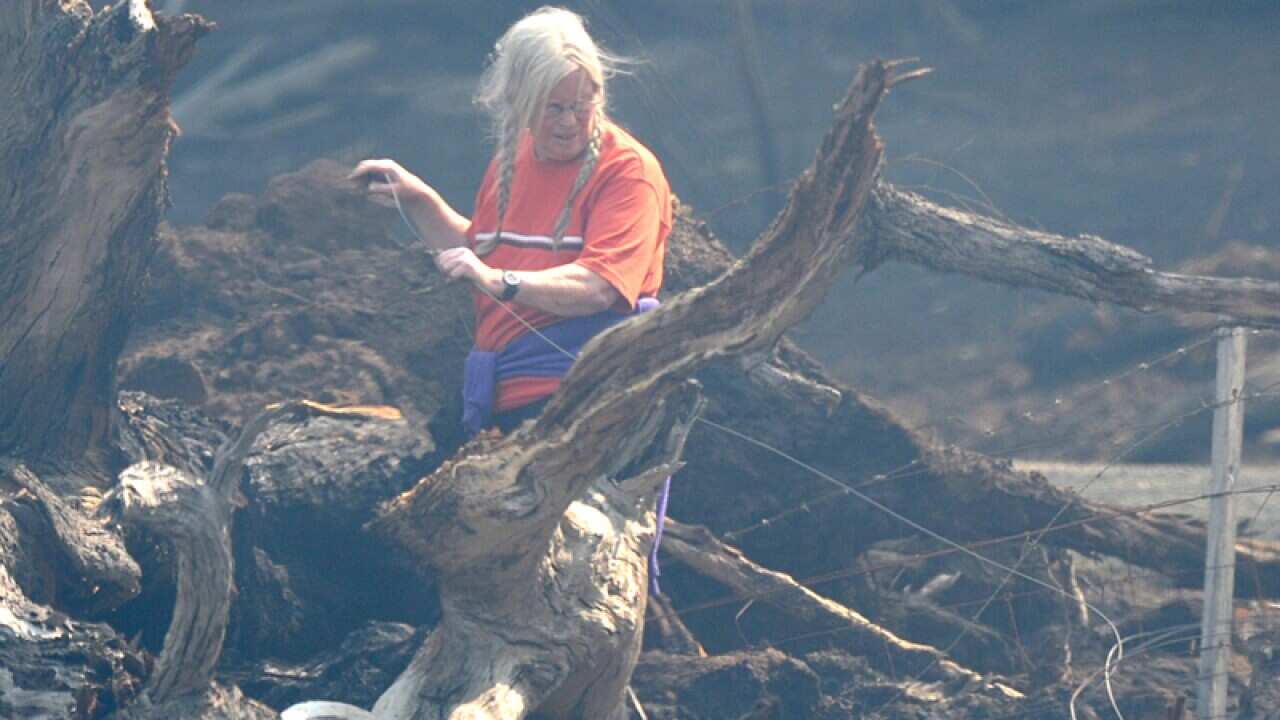 A resident attempts to fix her fence after a fast moving bushfire