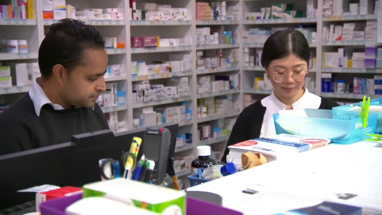 Chemists stand in front of shelves of medicines as they handle scripts from customers.