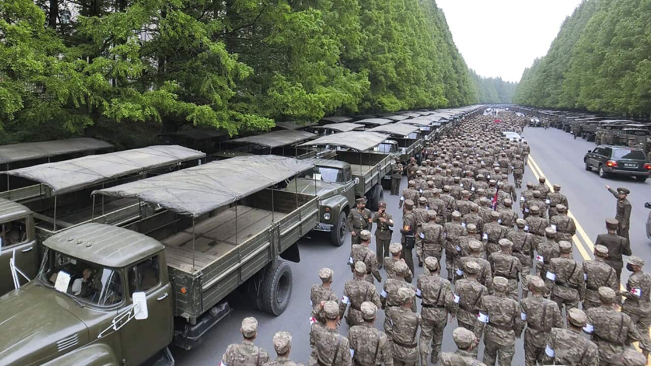 Army personnel are seen walking along a road where green trucks are parked.