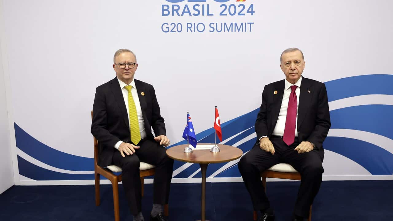 Turkish President Recep Tayyip Erdogan and Prime Minister Anthony Albanese sit beside each other at a G20 meeting. A small table with the Australian and Turkish flags is between them.