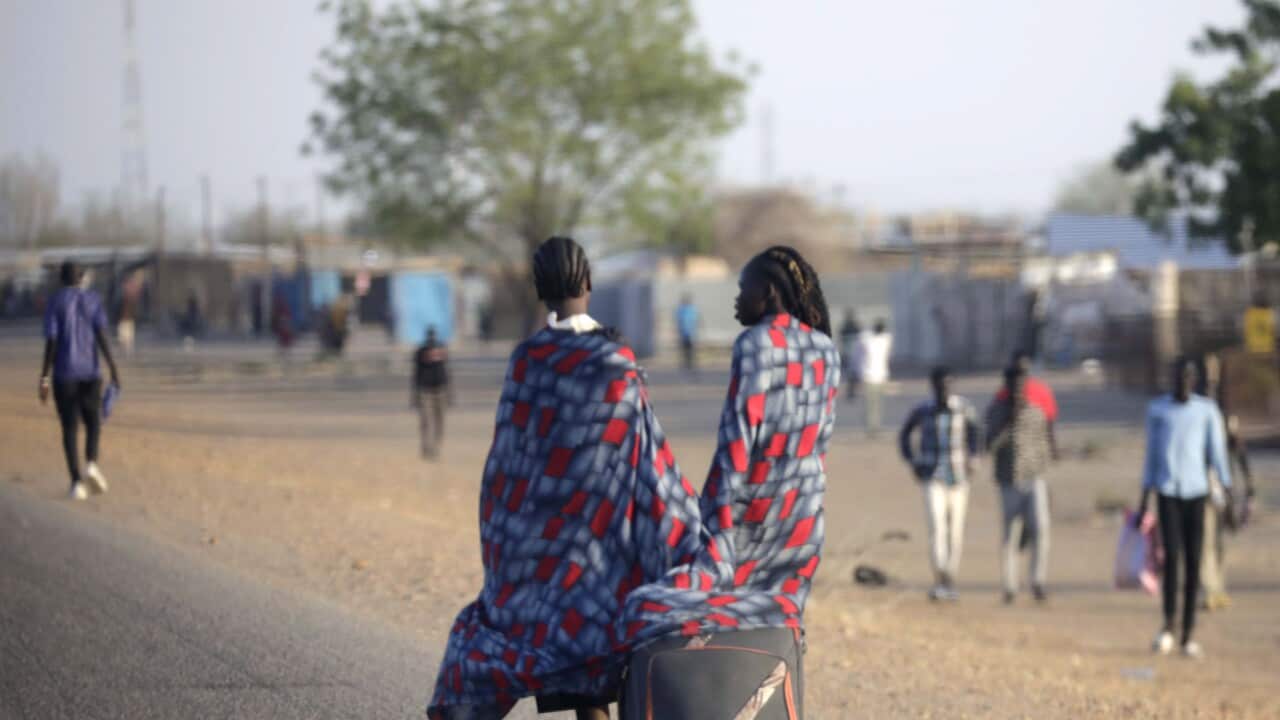 Two people pull a suitcase as they walk.