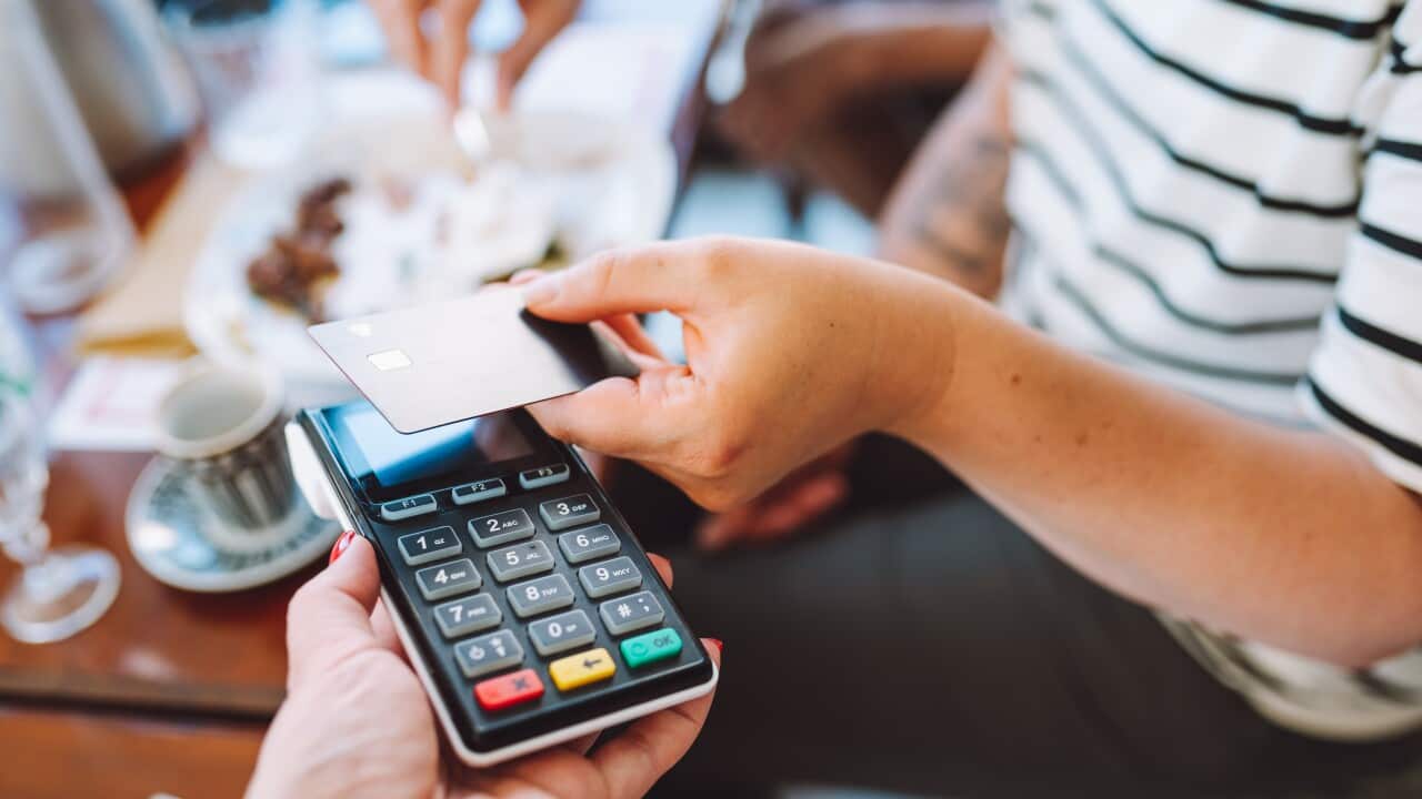 Cropped woman hand holding credit card to pay in cafe for food and drinks. Focus on hand and card reader. Close up