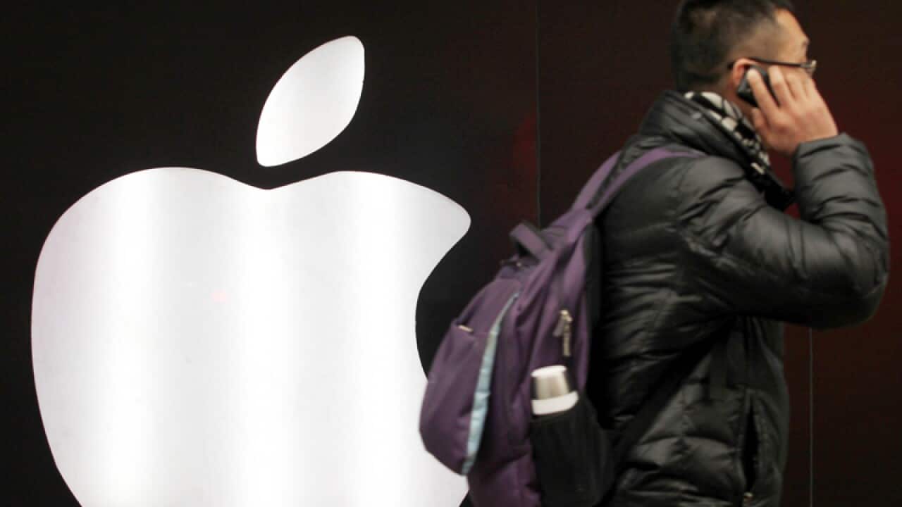 A man using his phone as he walks past the Apple logo