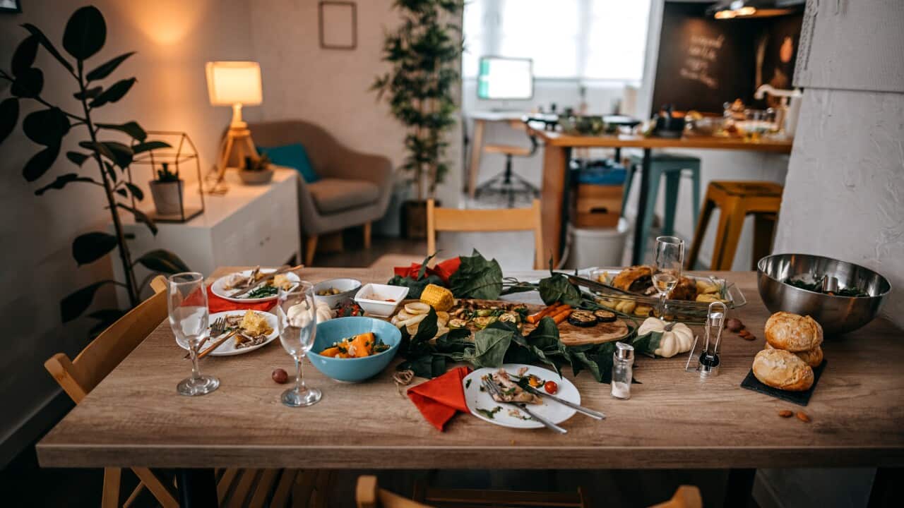 Dining table with leftover food, plates, glasses and vegetables after a shared meal.
