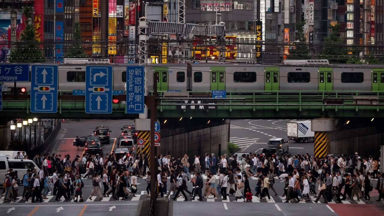 A large crowd passes a crossing as a commuter train travels overhead in the Shinjuku district of Tokyo.