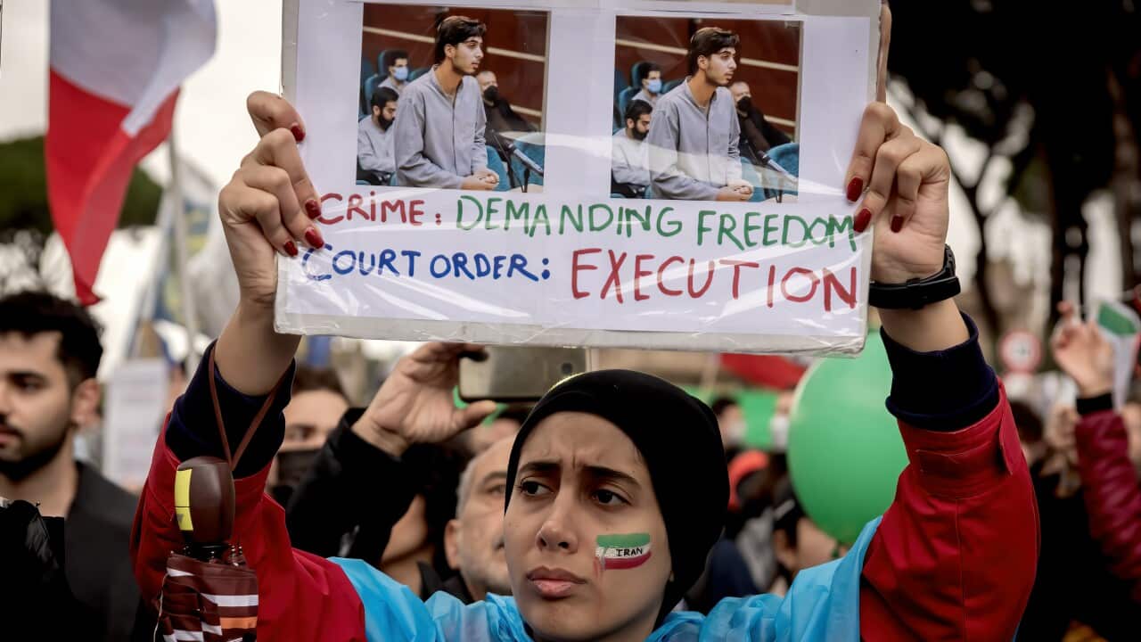 A woman with the Iranian flag painted on her face holds up a sign at a rally in Rome