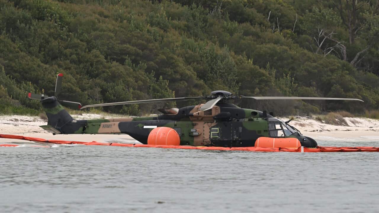A helicopter sits in water near a beach
