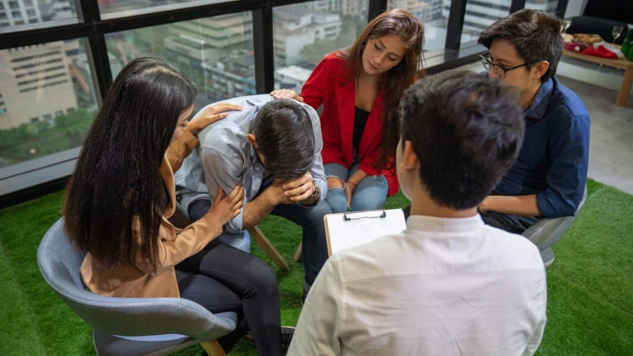 Group of young people sitting in a circle and talking to psychiatrist during a therapy