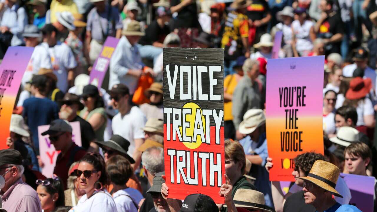 People stand in a crowd holding signs supporting the Voice to Parliament