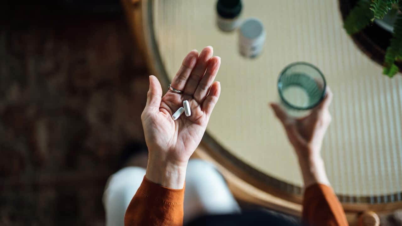 A woman taking medicines in hand with a glass of water at home.