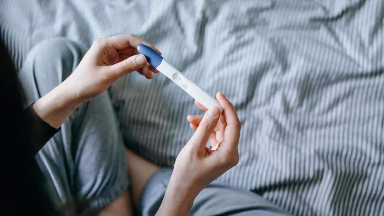High angle view of disappointed young woman sitting on the bed and holding a negative pregnancy test.