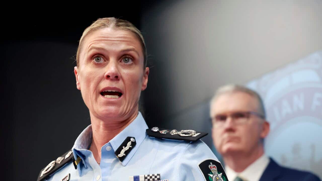 A police officer speaks with a man standing in the background