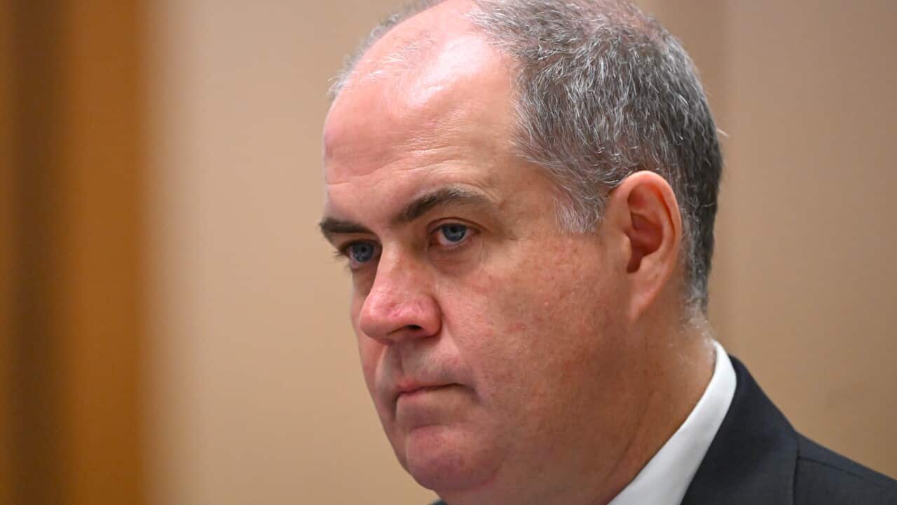 A bald man in a suit looks solemn.