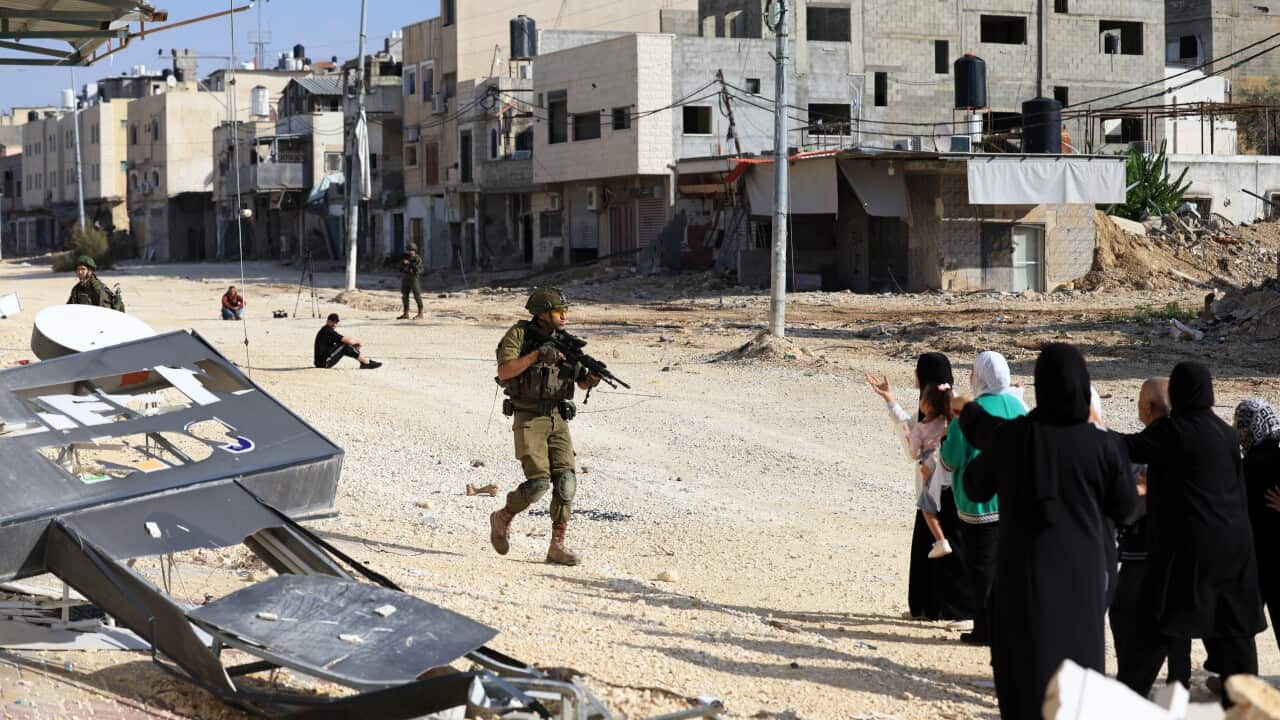 A soldier with a gun near a group of people, some of whom have their hands raised.