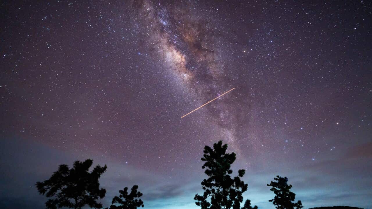 The illuminated path of a meteor in the night sky, against a silhouetted landscape.
