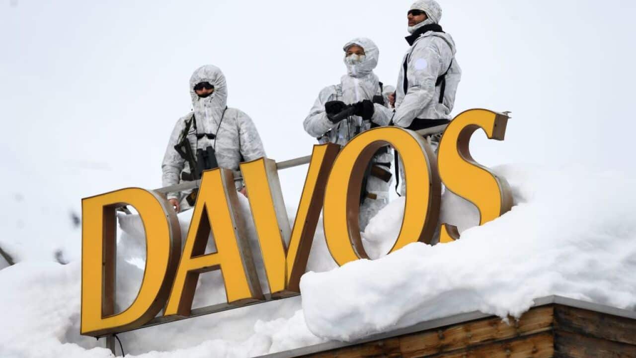 Three armed men dressed in white on a snow-covered roof, standing behind a large sign that reads Davos.